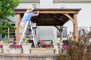 Man,staining,a,backyard,wooden,gazebo,behind,his,house,standing