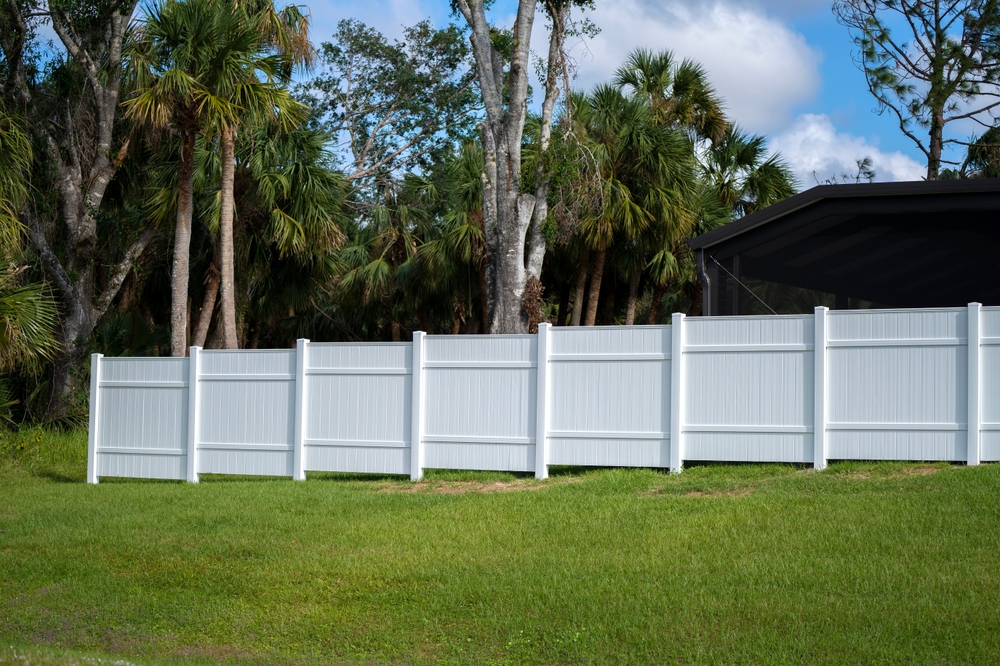 White,vinyl,picket,fence,on,green,lawn,surrounding,property,grounds