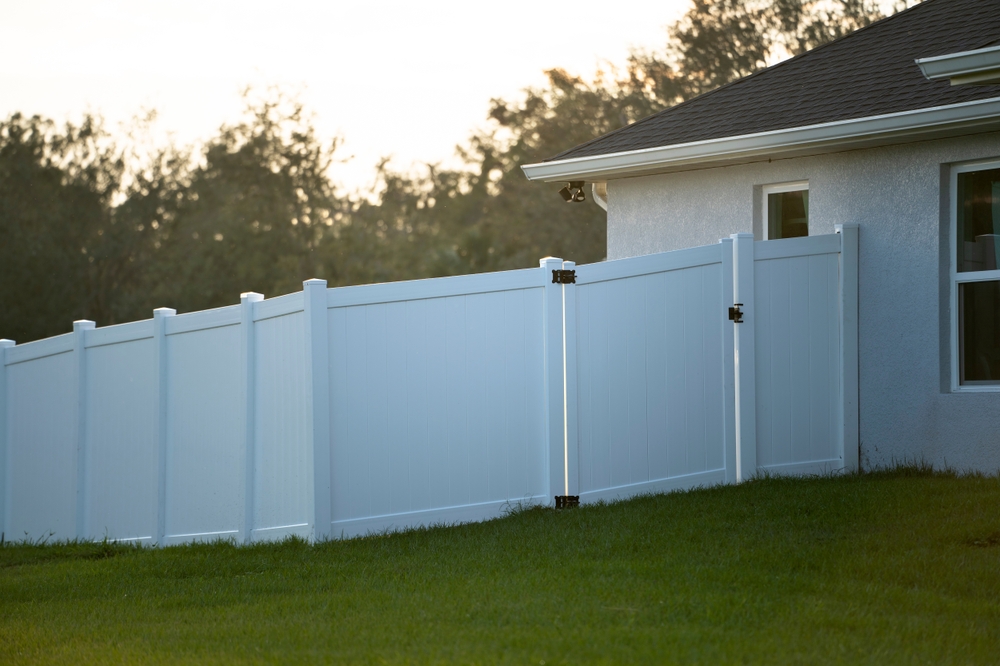 White,vinyl,picket,fence,on,green,lawn,surrounding,property,grounds