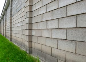 The,wall,of,cinder,block,fence,near,the,green,lawn.